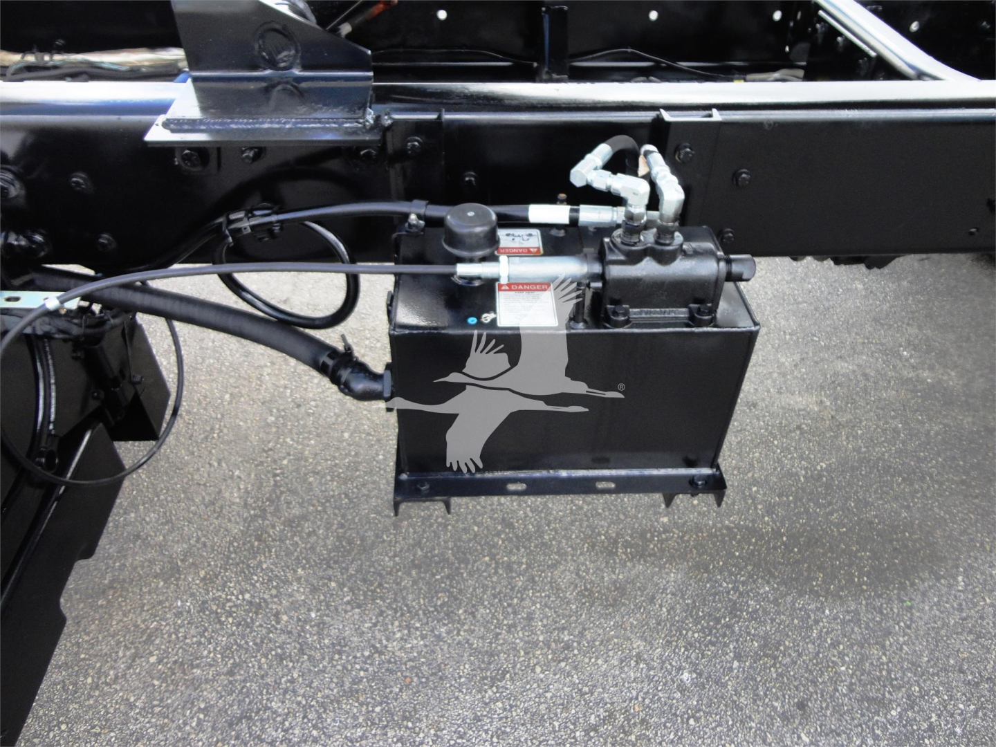 Freightliner M2 106 chassis showing hydraulic reservoir and pump assembly with hoses and fittings.