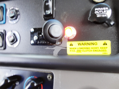Cab controls and warning label inside a Freightliner M2 106 dashboard area showing ignition switch, power outlet, warning sticker, and control knobs.