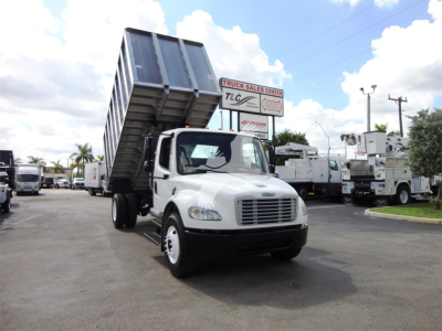 Truck with raised tipping bed in a dealership lot showing Freightliner M2 106 cab and dump bed raised