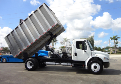 Truck chassis with a raised dump bed on a white Freightliner M2 106 dump truck, side view showing cab, hydraulic system, and dumping bed.