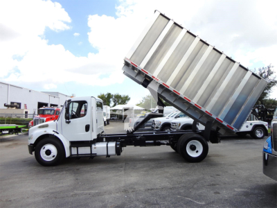 Freightliner M2 106 dump truck chassis with raised dump bed in a dealership lot.