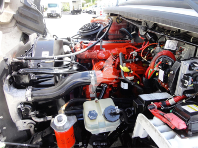 Engine bay of a 2014 Freightliner M2 106 showing bright red engine with surrounding hoses, reservoirs, and wiring harnesses.