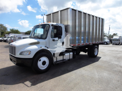 Freightliner M2 106 medium-duty truck with silver dump body, left-front view in a dealership lot.