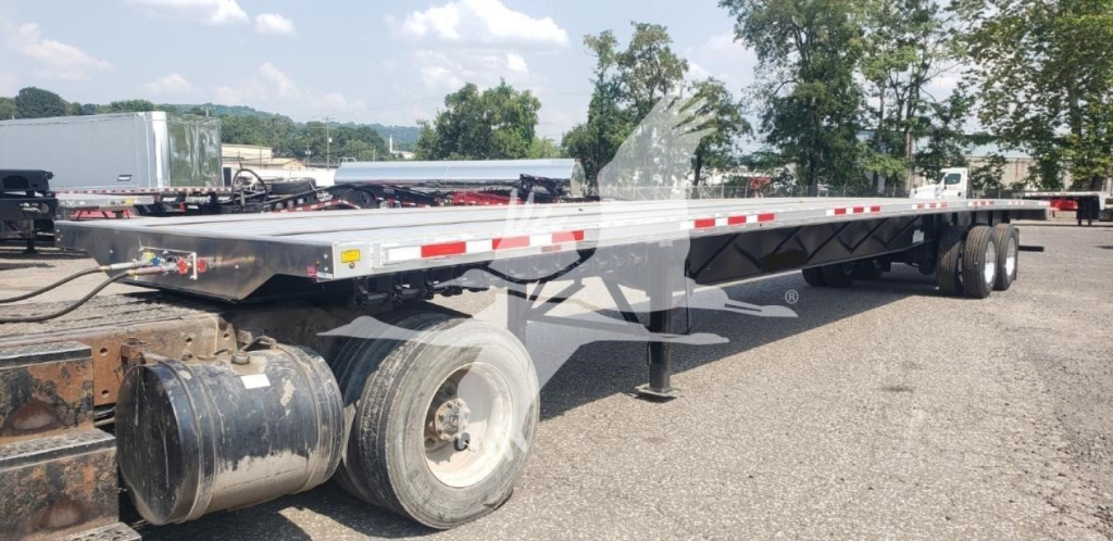 Flatbed trailer showing Fontaine combo flatbed with dual rear axles and support legs; visible tires, aluminum deck, and side reflectors.
