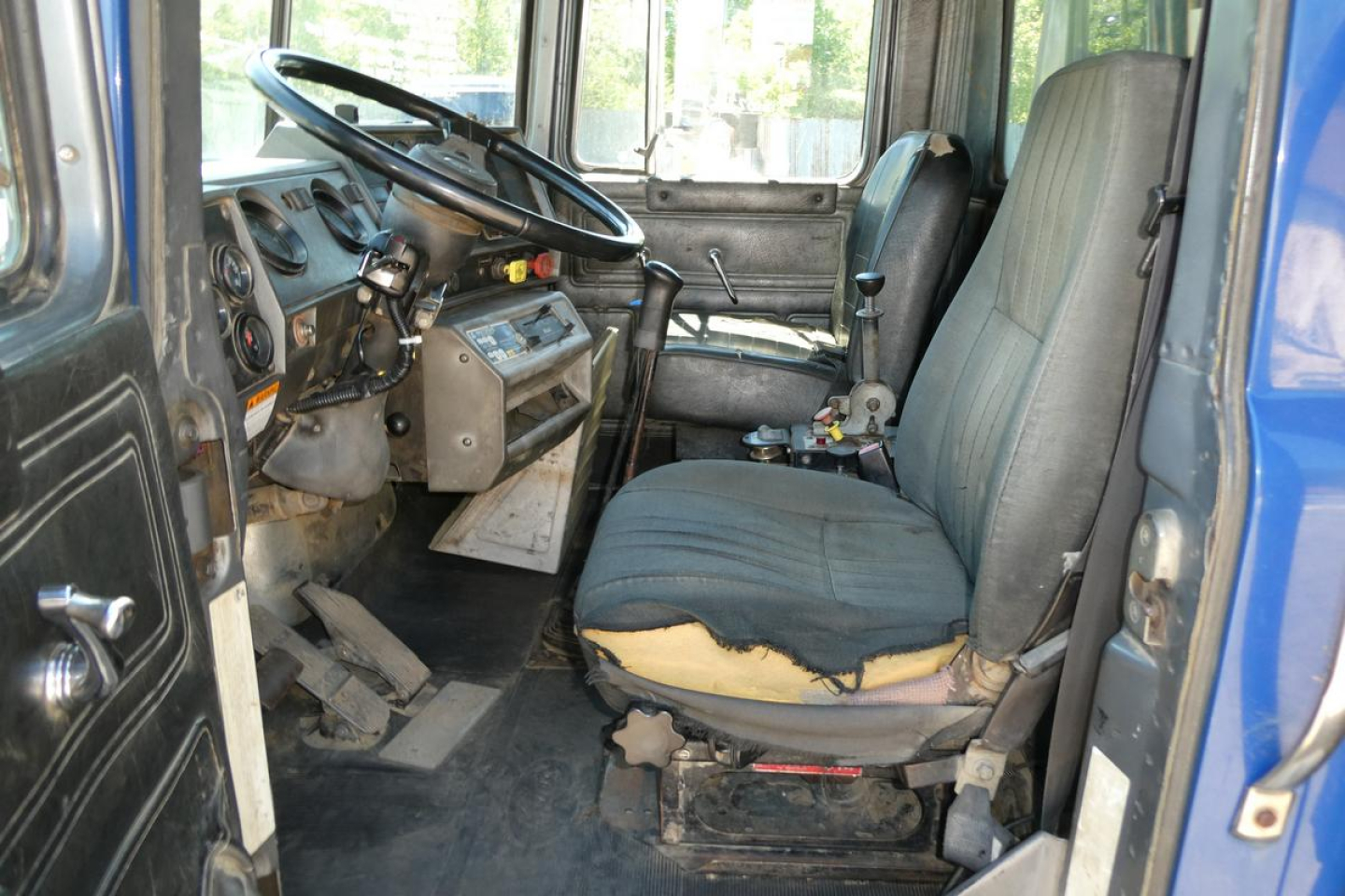 Truck cab interior of a 1998 Mack RD690S with worn driver seat and basic dashboard, steering wheel, gearshift, and pedals visible.