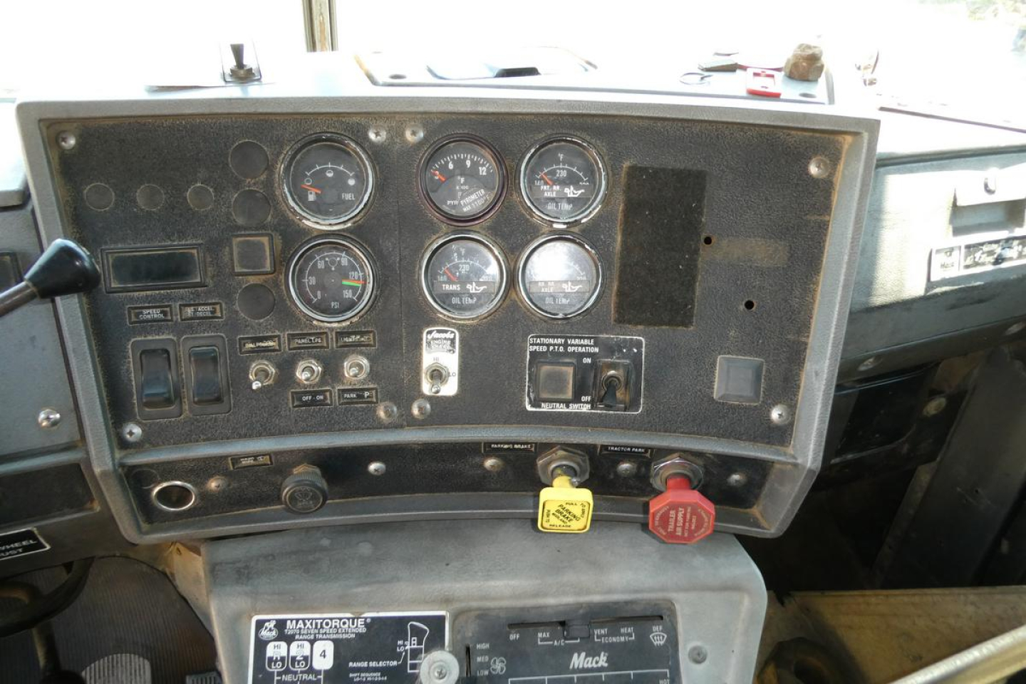 Dashboard of a Mack RD690S showing multiple gauges, switches, and warning labels in the instrument panel.