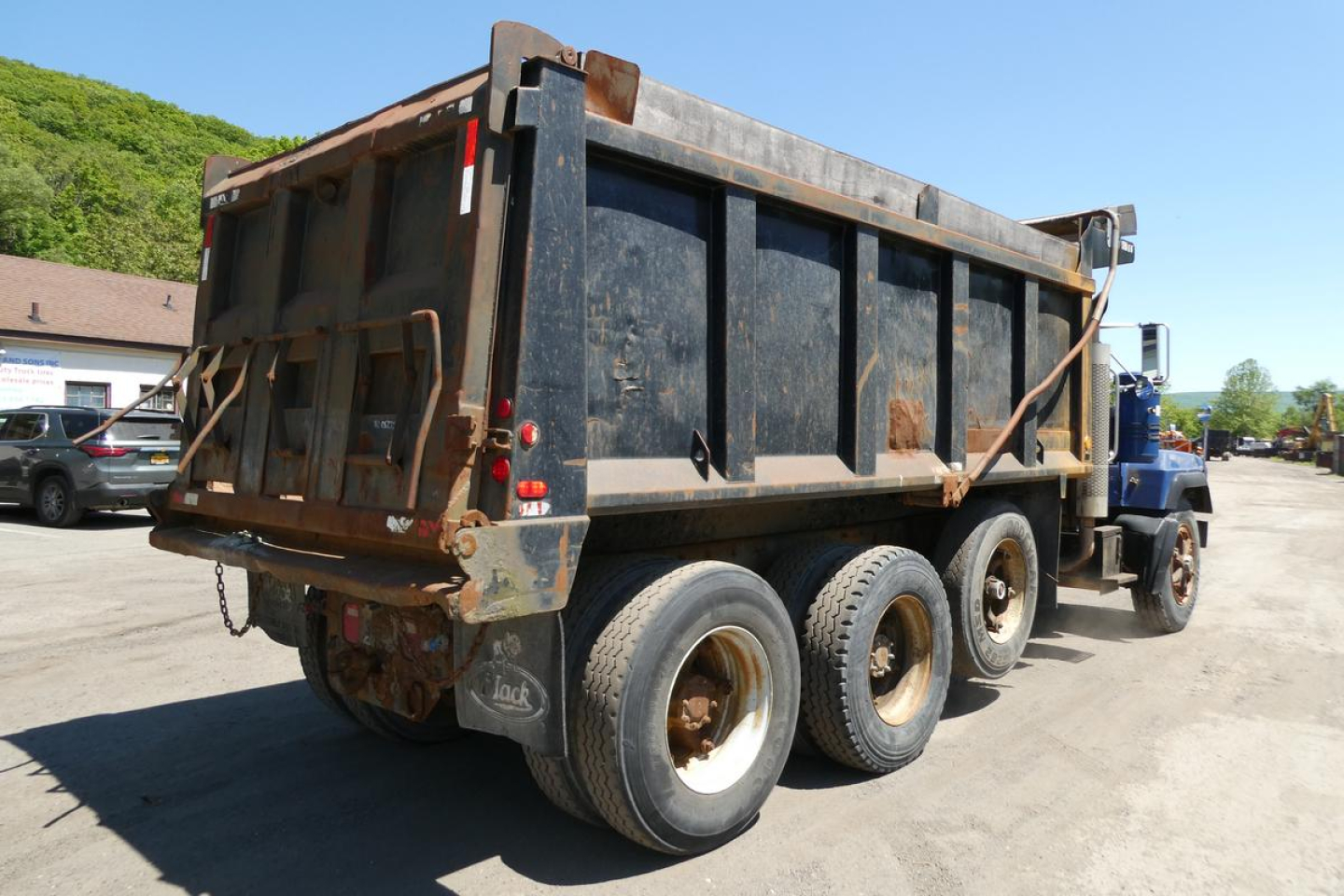 Mack RD690S dump truck rear view showing dump bed and triple-axle rear wheels, black bed panels, dirt and wear on container.