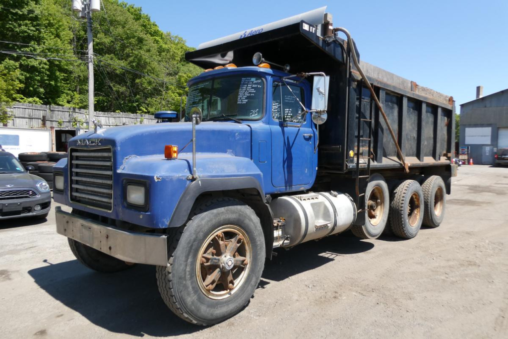 Mack RD690S dump truck in service showing blue cab and black dump bed with sleeper cab and dual rear axles.