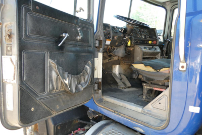Cab interior of a Mack RD690S dump truck showing steering wheel, dashboard, and driver door with control panel and seat.