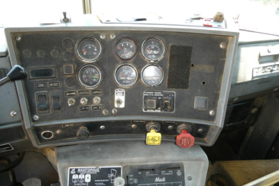 Dashboard of a Mack RD690S showing multiple gauges, switches, and warning labels in the instrument panel.
