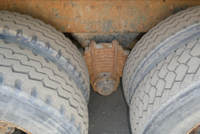 Mack RD690S dump truck rear axle view showing dual rear tires with rusty differential end and leaf spring hanger.