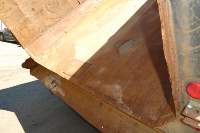 Dump truck bed with rusted steel side showing large open bed and hydraulic mechanism visible at edge.