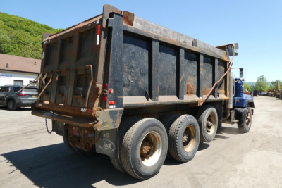 Mack RD690S dump truck rear view showing dump bed and triple-axle rear wheels, black bed panels, dirt and wear on container.