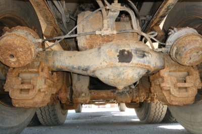 Dump truck rear suspension undercarriage showing solid axle, differential housing, and rust-free-looking components seen from ground-level view