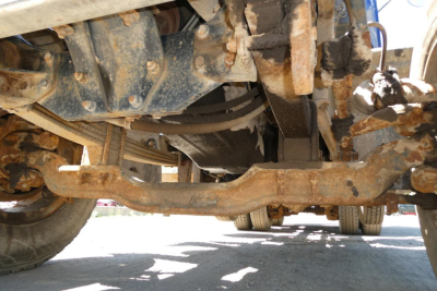 Underbelly of a Mack RD690S dump truck showing frame, suspension, and drivetrain components with rust and dirt.