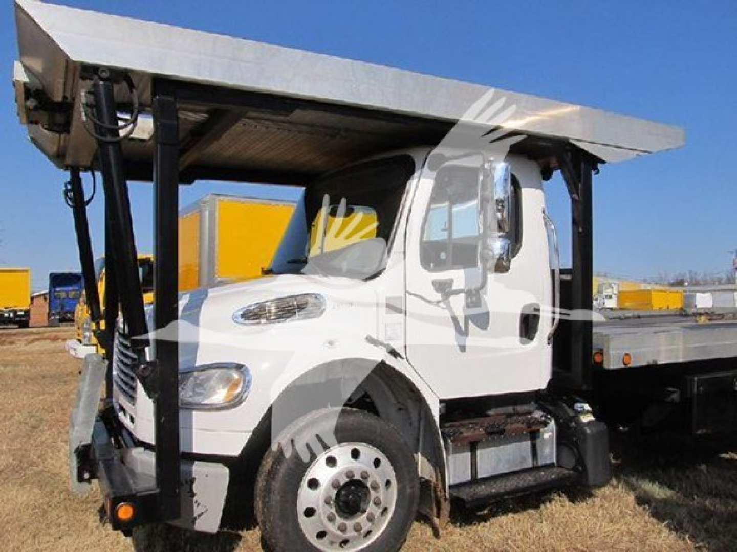 Truck cab of a Freightliner M2 106 with a flatbed trailer and hoist, side view showing front wheel and door, VIN and stock not visible on image