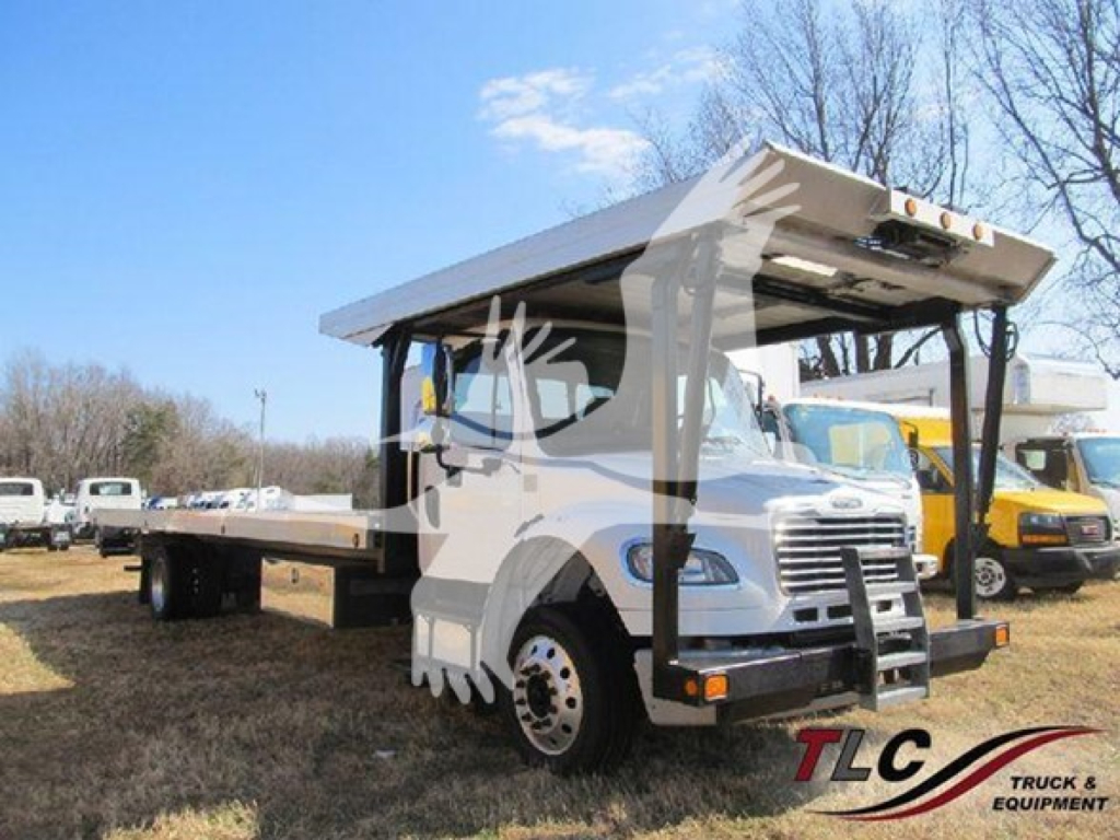 Truck cab and flatbed carrier with raised hoist on Freightliner M2 106, side view showing white body and equipment; stock TD5405 and VIN visible in listing