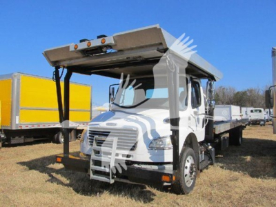 Flatbed tow truck with hydraulic lift, front grille, cab, and extended boom in service lot.