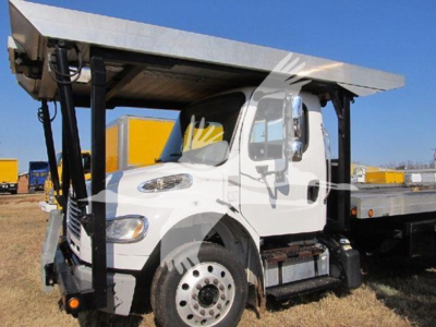 Truck cab of a Freightliner M2 106 with a flatbed trailer and hoist, side view showing front wheel and door, VIN and stock not visible on image
