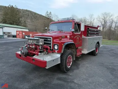 1980 International S1824 Pumper Truck fire engine side view showing front pump with hoses, chrome equipment, red body with silver diamond plate compartments, and towing wheels.