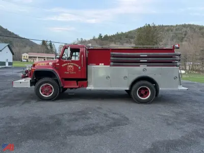 Fire engine side view showing red International S1824 pumper truck with chrome compartments and text on the door. Visible markings include small decals on the cab door and on the front fender.