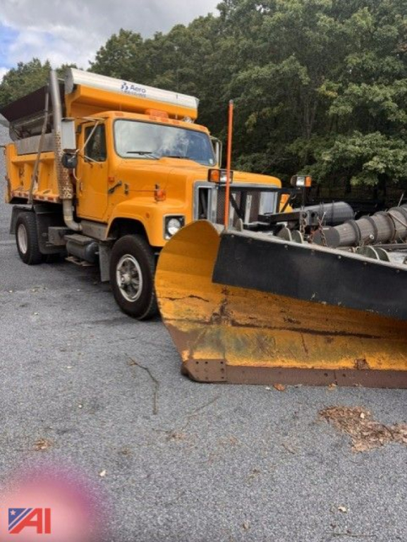 International 2574 dump truck with orange plow and sander equipment attached, side view in a gravel lot.