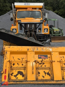 Front view of an orange 1993 international 2574 dump truck with a snow plow attachment in a yard of gravel piles.