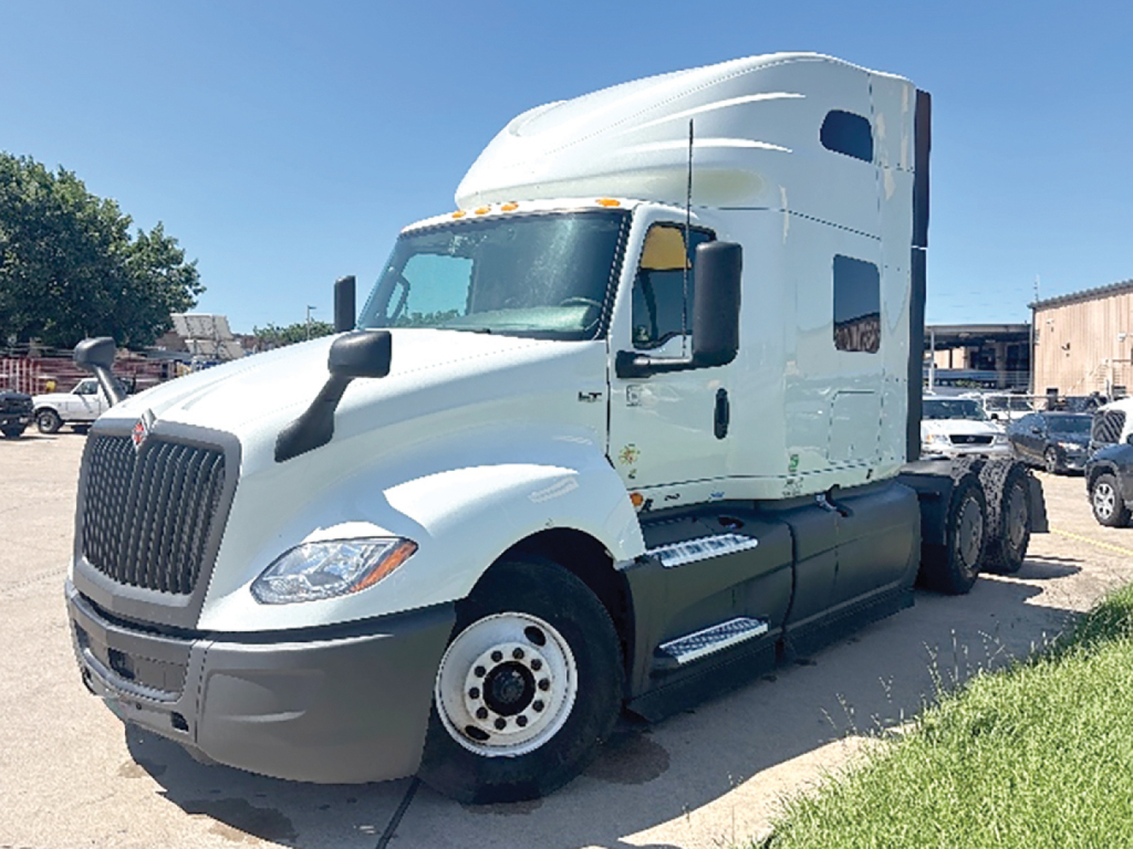 Truck cab showing International LT625 sleeper tractor, white exterior, front grille, single rear axle, side steps, and VIN label visible