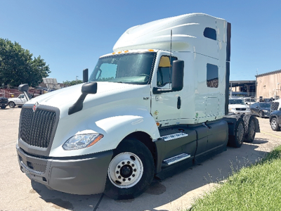Truck cab showing International LT625 sleeper tractor, white exterior, front grille, single rear axle, side steps, and VIN label visible