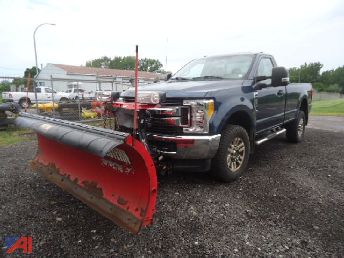 Ford F-350 Super Duty pickup truck with a red snow plow attached, dark blue exterior, extended cab, four-wheel drive, parked on gravel.