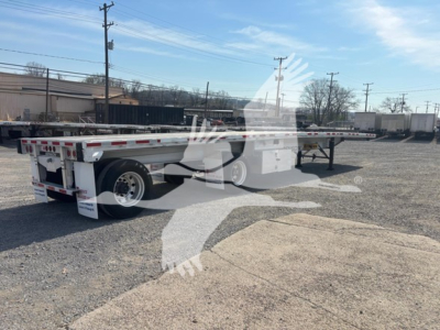 Flatbed trailer showing dual rear axles and reflective tape with text on mudflaps and rear bumper; VIN and stock number not visible on this view.