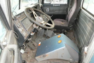 Cab interior of a 1988 Peterbilt 377 showing worn steering wheel, dashboard, and a blue metal console in the cab area.