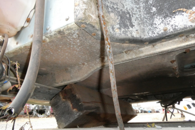 Truck undercarriage showing rusted frame and drivetrain area with rusted crossmember and wiring near Peterbilt 377; some peeling paint.