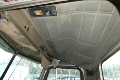 Cab interior of a Peterbilt truck showing overhead headliner, control panel, and sun visor area with worn fabric; text on stickers/buttons not clearly legible.
