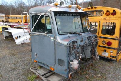 Truck cab front view with exposed engine bay, blue-gray cab, dual mirrors, and multiple warning lights on top; visible damaged front end and wiring harnesses.