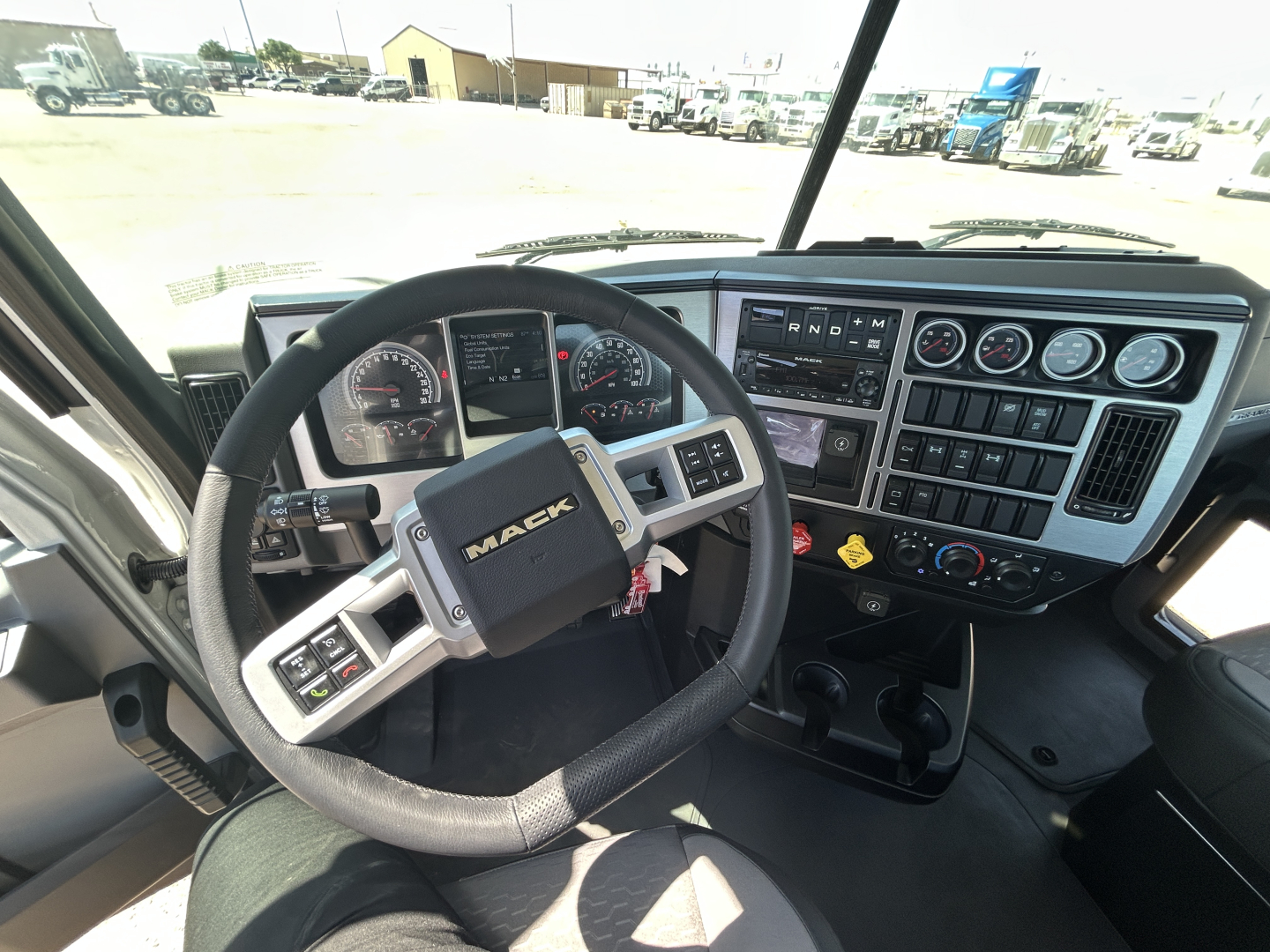 Interior of a 2027 Mack GR64FT truck cab showing steering wheel with MACK logo, dashboard with multiple gauges, controls, and gear selector.