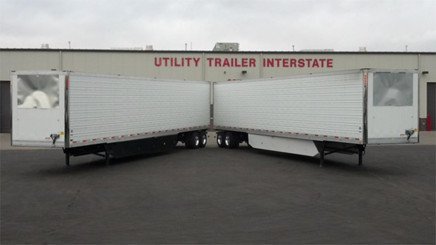Trailer bay showing two joined Utility Reefer trailers with closed white side panels and red lettering Utility Trailer Interstate on the building behind.