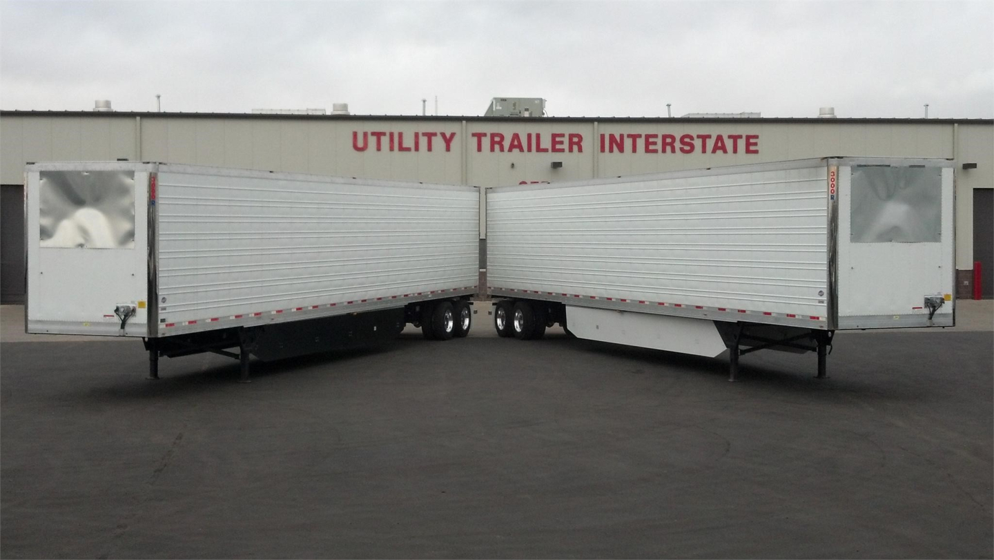 Two Utility trailer reefer units aligned nose-to-nose in a lot with a building that reads 'Utility Trailer Interstate' in red letters.