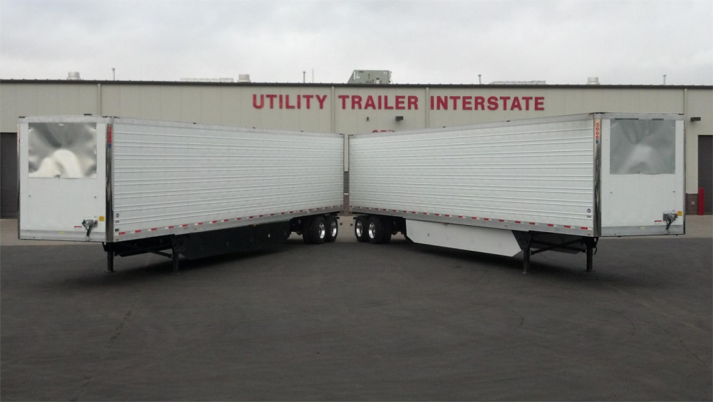 Two Utility trailer reefer units aligned nose-to-nose in a lot with a building that reads 'Utility Trailer Interstate' in red letters.