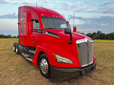 2024 Kenworth T680 red tractor-trailer in a field, chrome grille, large windshield, dual side mirrors.