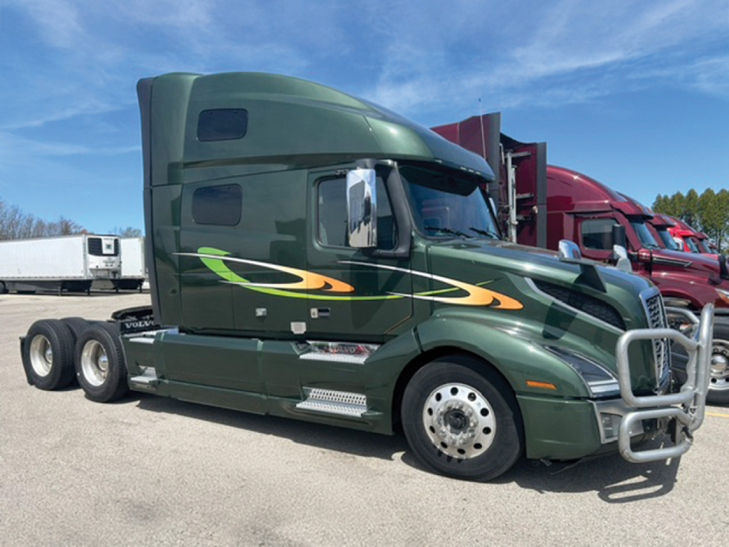 Volvo VNL 760 sleeper cab truck showing green exterior with orange and yellow graphics and chrome bumper guard.