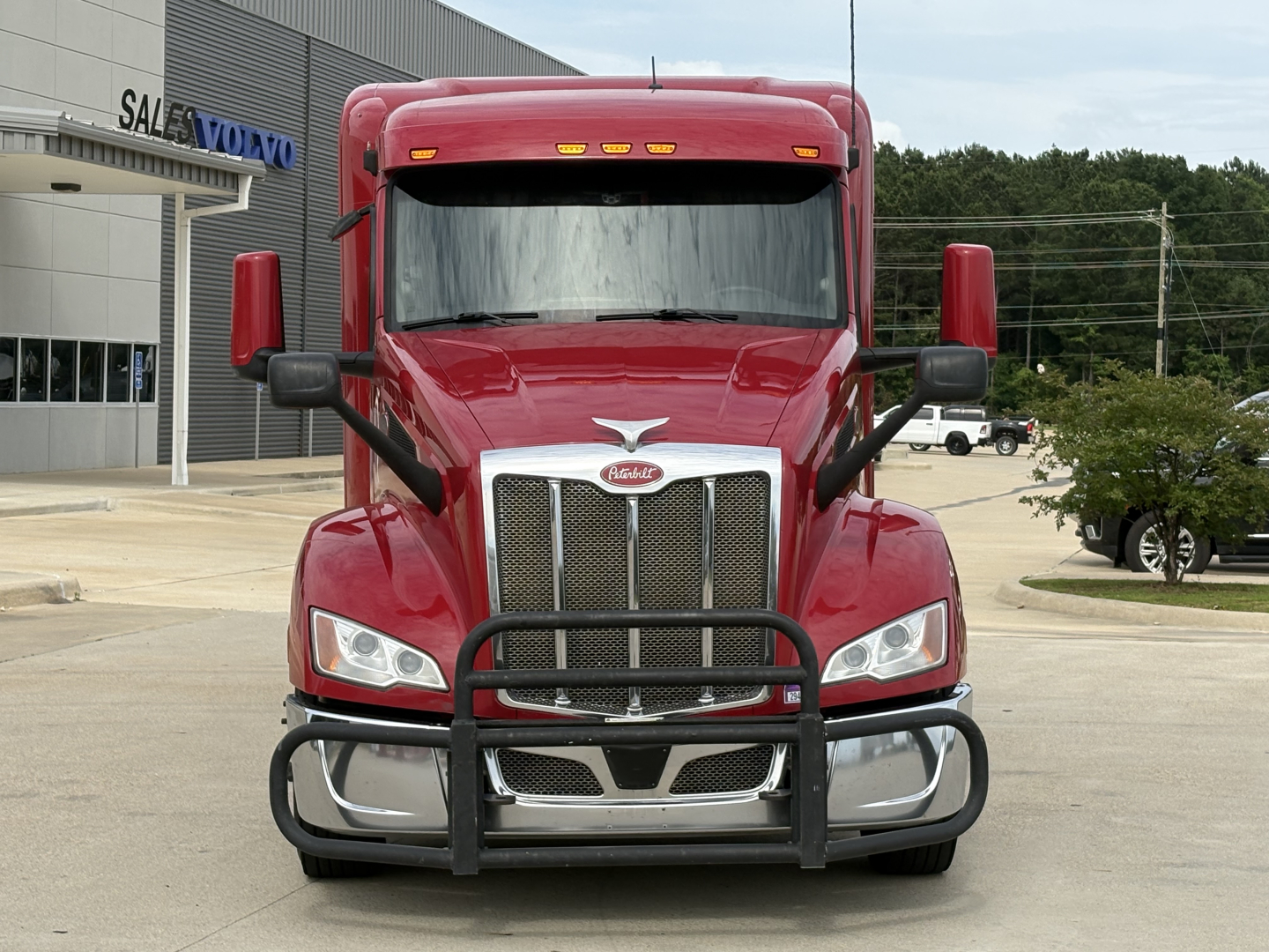Peterbilt 579 cab front view showing grille guard, red exterior, side mirrors, and headlamps in a dealership lot.