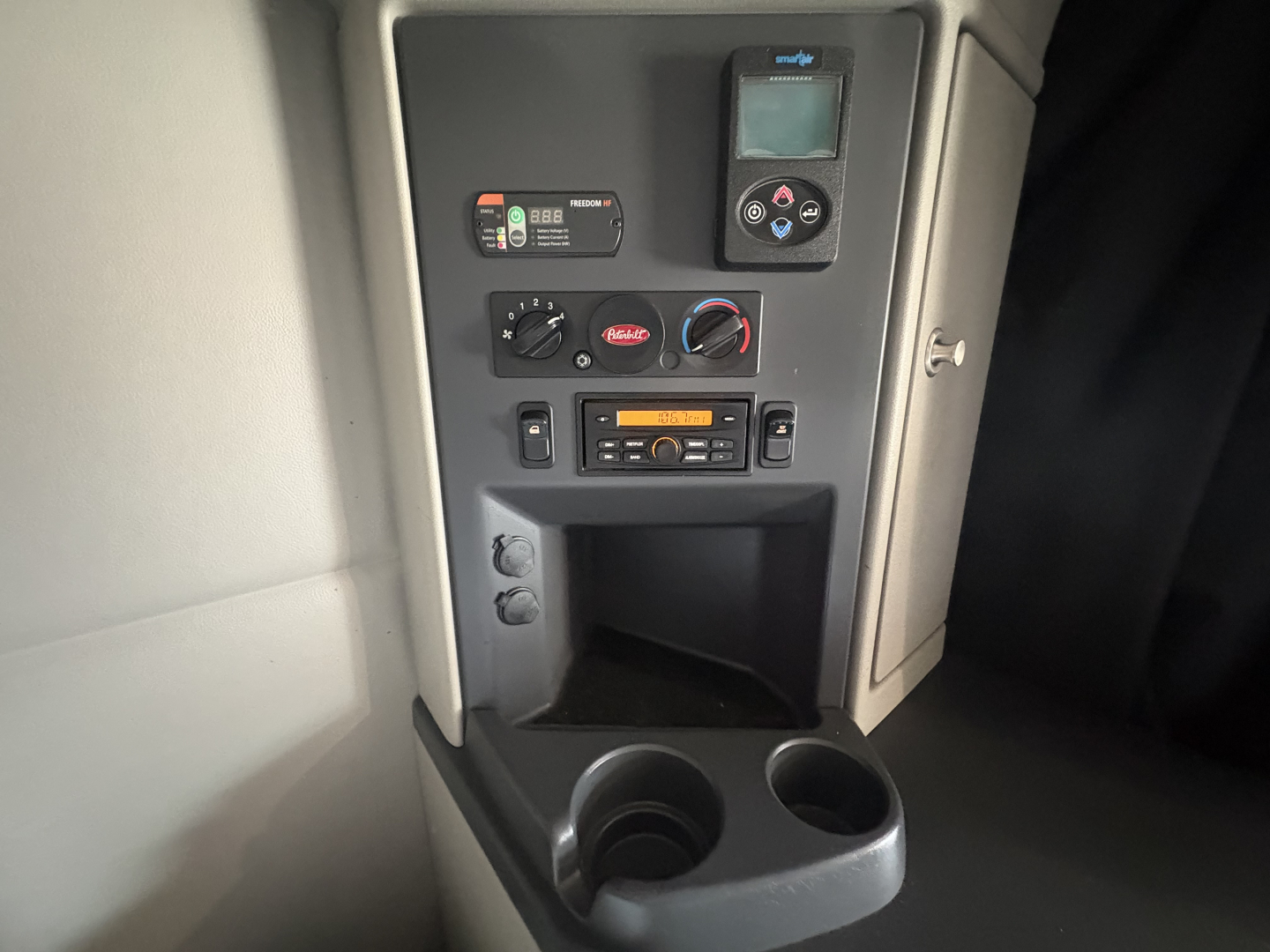 Vehicle cab interior panel showing controls, display screen, radio, climate dials, and cup holders.