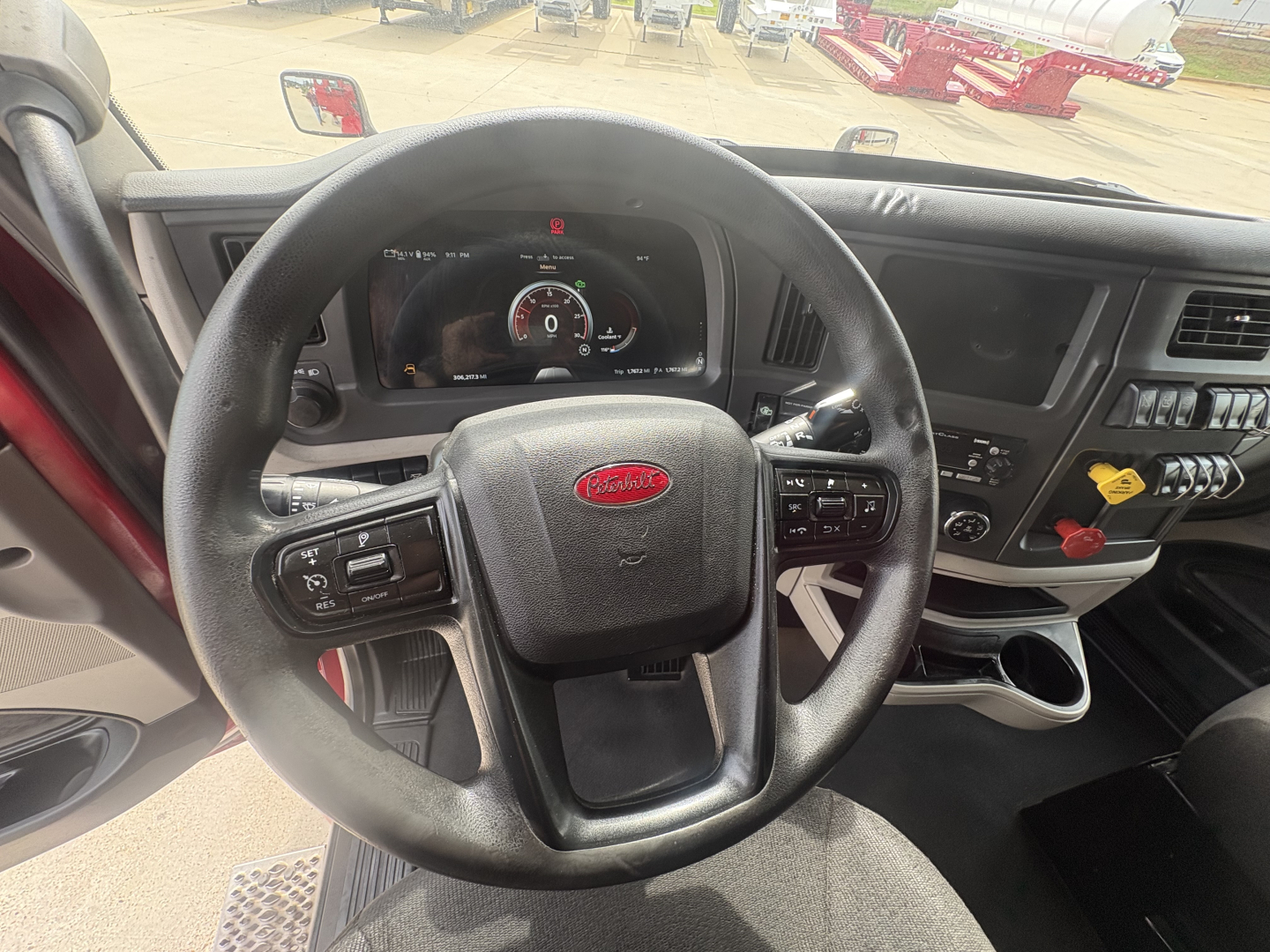 Peterbilt truck steering wheel and dashboard interior with digital gauge cluster, various controls, and cup holder visible.