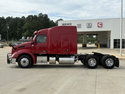 Peterbilt 579 tractor-trailer cab in red side view with service center in background.