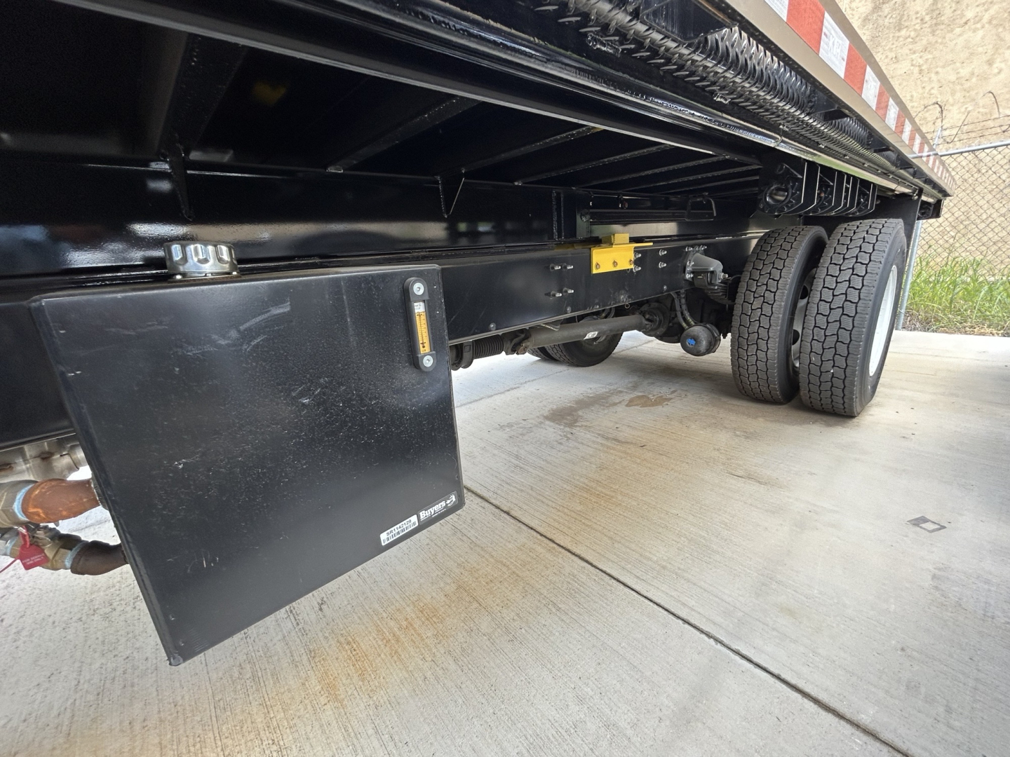 Mack MD6 chassis side showing flatbed with undercarriage components and a black toolboxmounted near the trailer frame.