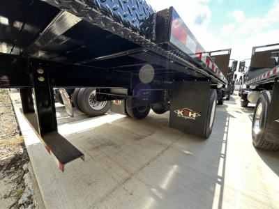 Flatbed truck undercarriage of a 2026 Mack MD6 showing black steel frame, hydraulic components, and a KWH Industries mud flap. 