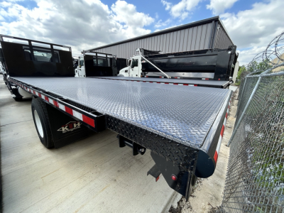 Flatbed truck bed on a 2026 Mack MD6 showing diamond plate deck and rear bumper with tail lights and hitch crossbeam.