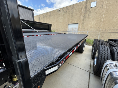 Mack MD6 flatbed truck chassis with diamond plate steel deck and dual rear axles, side view showing flatbed surface and wheel area.