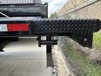 Flatbed trailer rear-left side of a 2026 Mack MD6 showing diamond plate steel step and extendable hitch with red reflector and K&N badge.